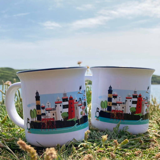 Two mugs with lighthouse design on grass with a scenic background