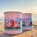 Two enamel mugs with coastal design on a beach at sunset