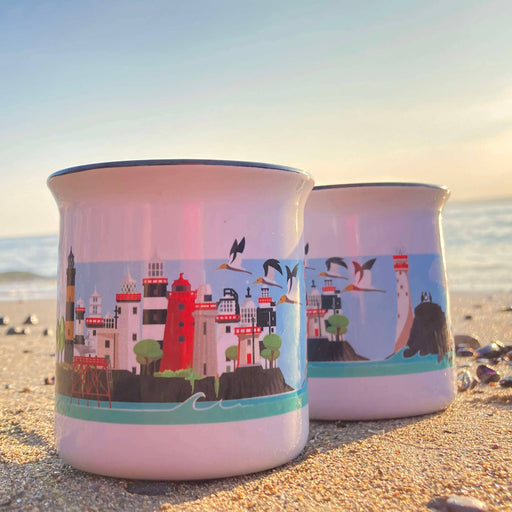 Two enamel mugs with coastal design on a beach at sunset