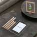 Round dark coffee table with deconstructed wooden frame with perspex sheet and paper featuring 'Chicura' logo on a textured floor.