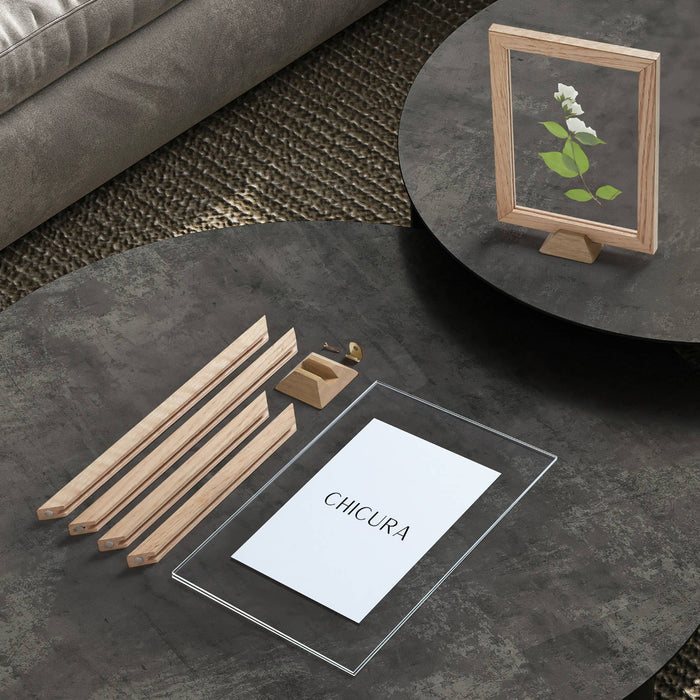 Round dark gray table with deconstructed wooden frame, a small plant, and a card on a textured surface.