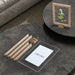 Round dark gray table with deconstructed wooden frame, a small plant, and a card on a textured surface.