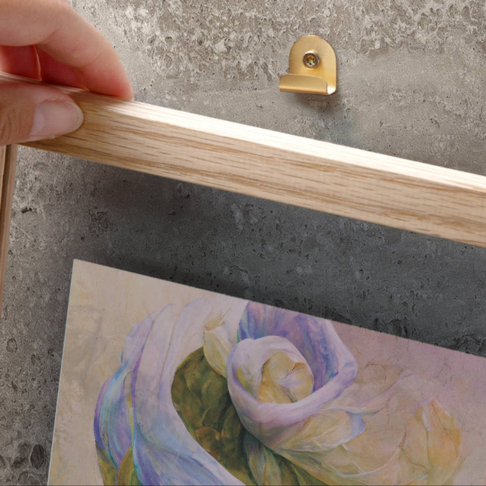 Hand holding a wooden frame with a metallic hook on a concrete surface with a painting of flowers.
