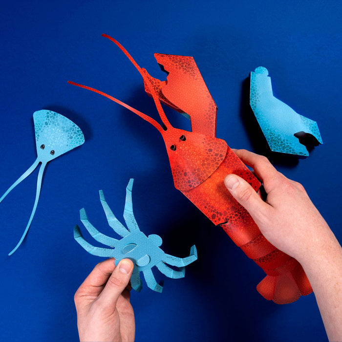 Red paper lobster and blue paper fish on a blue background