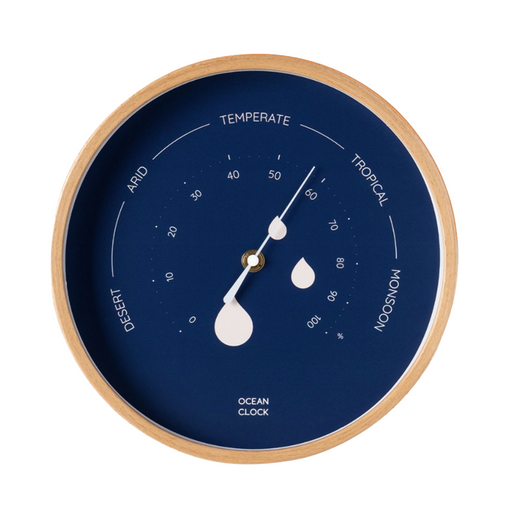 A round ocean clock with a light wood frame and a deep navy blue dial. The dial features white text and markings for temperature zones (Temperate, Tropical, Monsoon, Desert, Arid) and water droplet indicators, with white hands and a central gold accent.