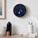 Wall clock on a white wall above a wooden surface with decorative items.