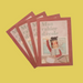 Four children's school notebooks with reddish-brown covers fanned out on a solid yellow background. The cover features a cute illustration of a pencil character writing in a notebook.