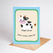 Greeting card with a cow illustration and 'Moo-chas Gracias' text on a beige background.