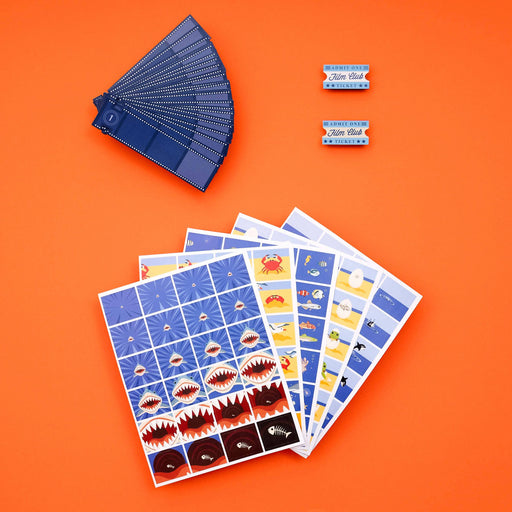 A set of blue-themed sticker sheets and two matching blue stickers displayed on a bright orange background. The sticker sheets feature cartoon shark teeth, fish, and other marine illustrations.