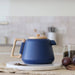 Blue teapot with wooden handle on a white surface, blurred kitchen background