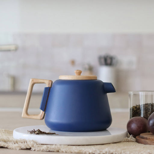Blue teapot with wooden handle on a white surface, blurred kitchen background