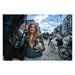 Woman with red hair holding a dog, standing next to a horse on a city street.