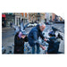 People feeding pigeons on a city street with buildings and traffic in the background