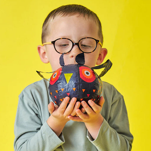boy blowing up owl paper balloon against yellow background