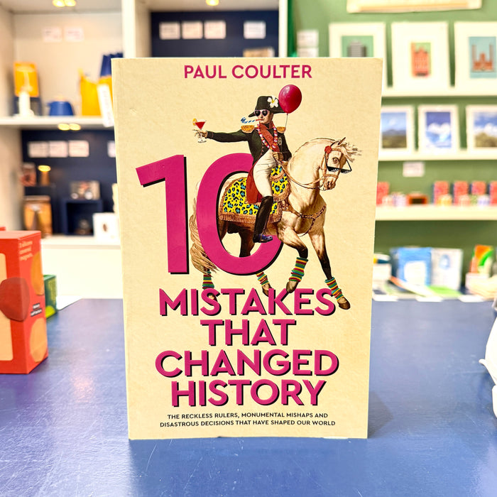 The book '10 Mistakes That Changed History' by Paul Coulter stands upright on a blue table. The cover features a vintage illustration of a rider on a horse with a large pink '10' and bold pink title text on a beige background.