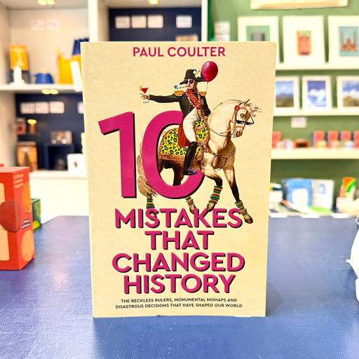 The book '10 Mistakes That Changed History' by Paul Coulter stands upright on a blue table. The cover features a vintage illustration of a rider on a horse with a large pink '10' and bold pink title text on a beige background.