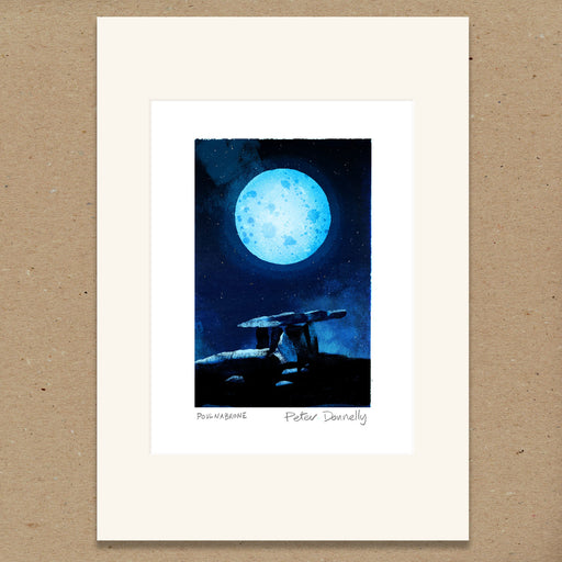 A matted art print featuring a dark blue night sky with a large glowing blue moon and a silhouetted figure on a hill. The print has an off-white mat border and the signature 'Peter Donnelly' with 'Poulnabrone' below, displayed against a brown textured background.