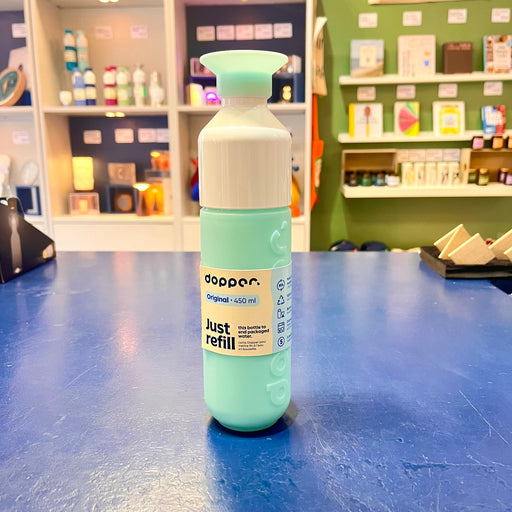 Light blue Dopper water bottle on a blue surface with shelves in the background