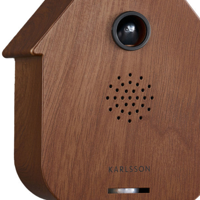 Wooden birdhouse-shaped device with a camera and speaker on a white background