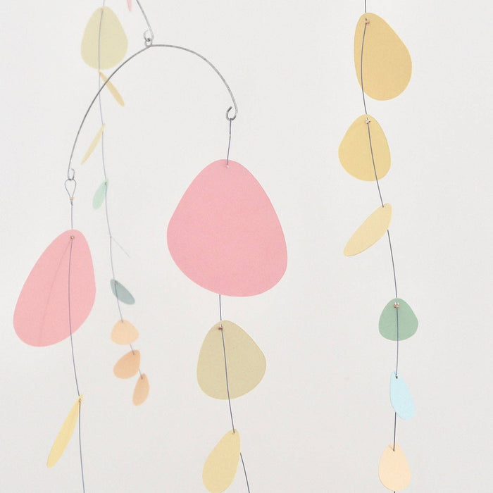 A minimalist mobile with thin metal wire arches and hanging organic-shaped paper pieces in pastel pink, yellow, peach, mint green, and light blue against a plain white background.