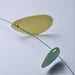 A close-up of a minimalist mobile or hanging sculpture with translucent oval discs suspended on a thin blue wire against a light gray background.