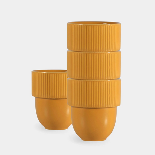 A set of mustard yellow ribbed ceramic cups, with one stack of three cups in front of a single cup, photographed on a light gray background.