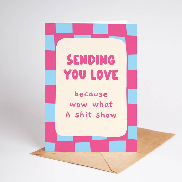 Greeting card with pink and blue checkered border and text 'Sending you love because wow what A shit show' on a white background.