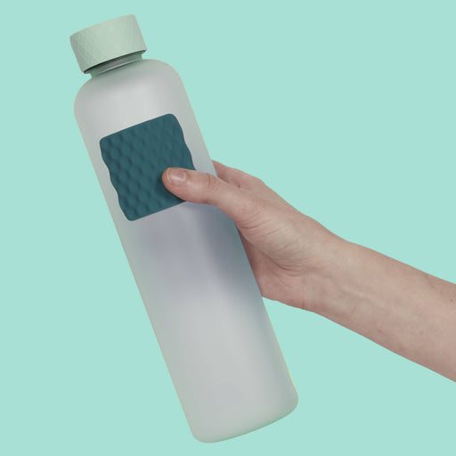 Hand holding a white water bottle with a textured green grip on a light blue background
