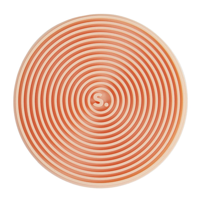 A round, top-down view of a peach-colored silicone mat with concentric circular grooves and a small white 'S.' logo in the center, set against a plain white background.