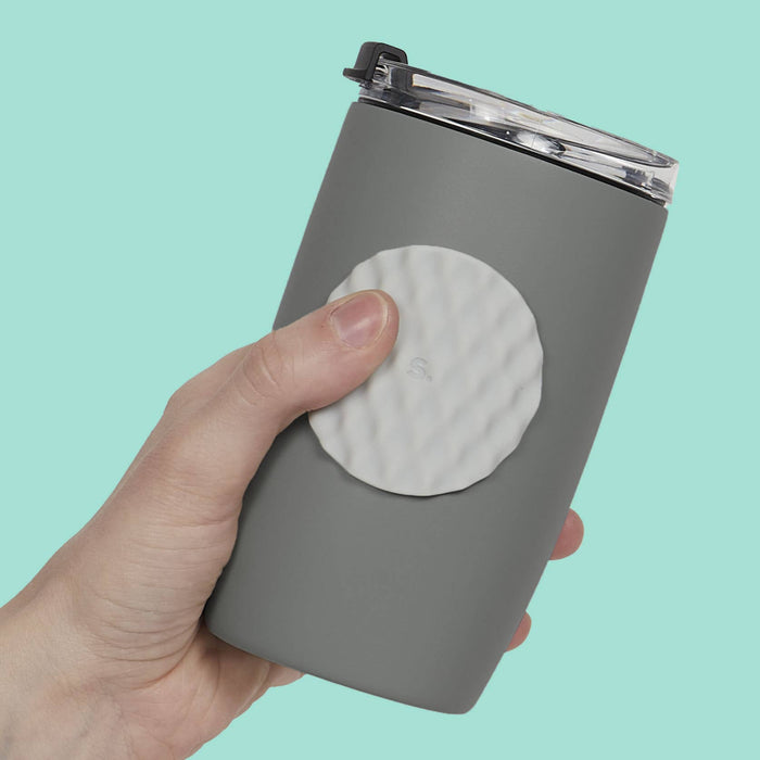 A hand holding a gray insulated tumbler with a clear lid and a circular textured white insert on the front, set against a solid mint green background.