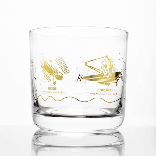 A clear glass rocks tumbler featuring gold foil illustrations of the Hubble and James Webb telescopes with their respective names printed below, set against a clean white background with a soft reflection.