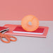 Orange ball on pink books with scissors on a light gray surface and pink background