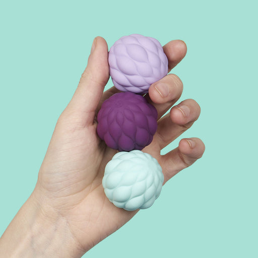 Hand holding three textured stress balls against a light blue background