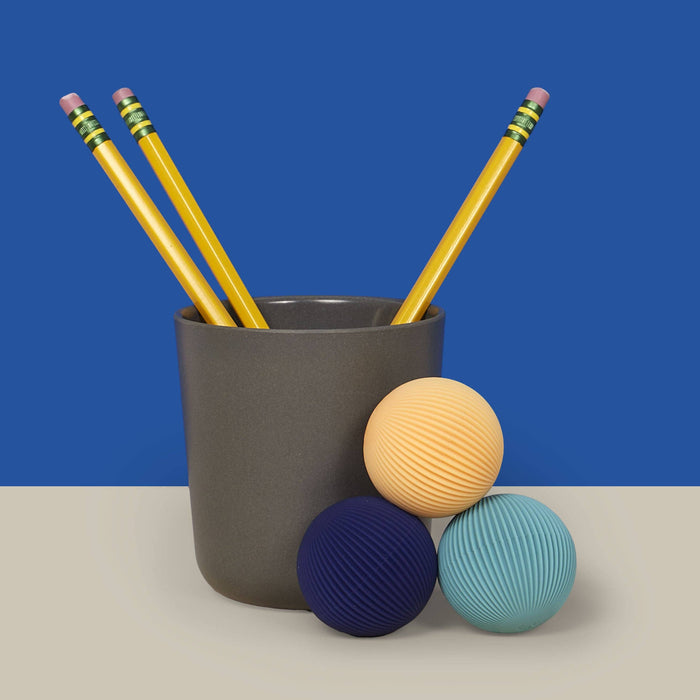 Gray cup with yellow pencils and colorful balls on a blue and beige background