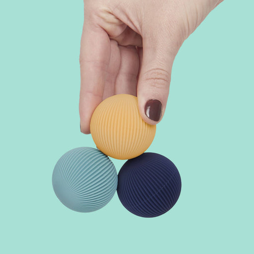 Hand holding three textured balls in yellow, blue, and purple against a light blue background