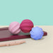 Three colorful silicone lip balm cases on a pink stand with a light blue background