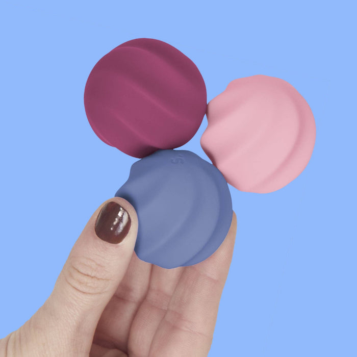 Three colorful lip balm tubes held by a hand against a blue background