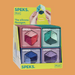 A retail display box of SPEKS. Pivot silicone flexagon toys, showing four colorful folded boxes in pink, mint, blue, and purple on a solid orange background.