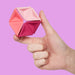 Hand holding a pink geometric object against a pink background