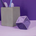 Concrete pencil holder with pens on a purple background, featuring a geometric purple object.