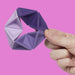 Purple and lavender geometric puzzle toy held by a hand against a pink background