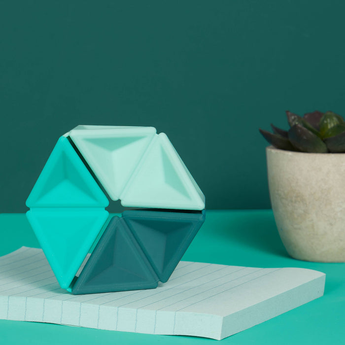 Geometric teal vase on a notebook with a plant in the background