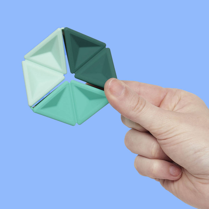 Hand holding a green geometric fidget spinner against a blue background