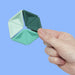 Hand holding a green geometric fidget spinner against a blue background