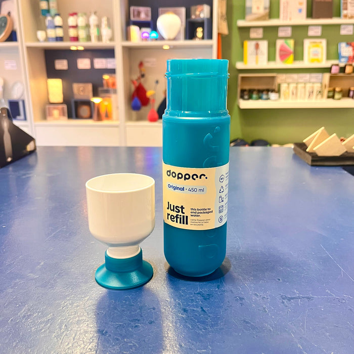 Teal water bottle with 'Dopper' branding and white cup on a blue surface.