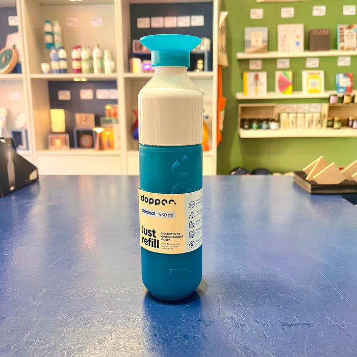 Teal and white reusable water bottle with 'Dopper' branding on a blue surface, store shelves in the background