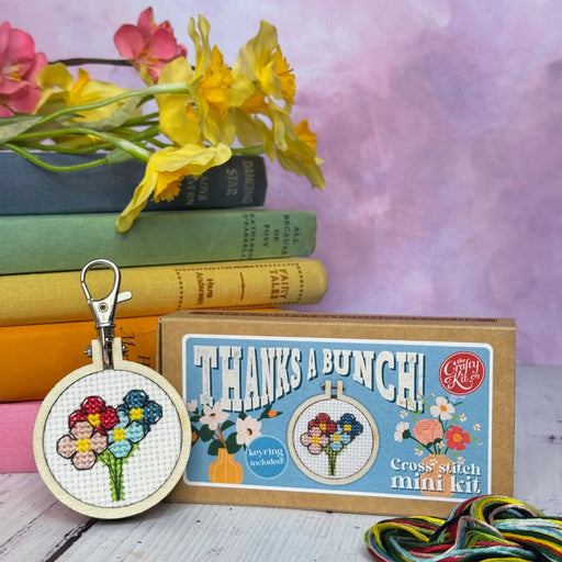 Cross stitch kit with floral design displayed in front of books and flowers 