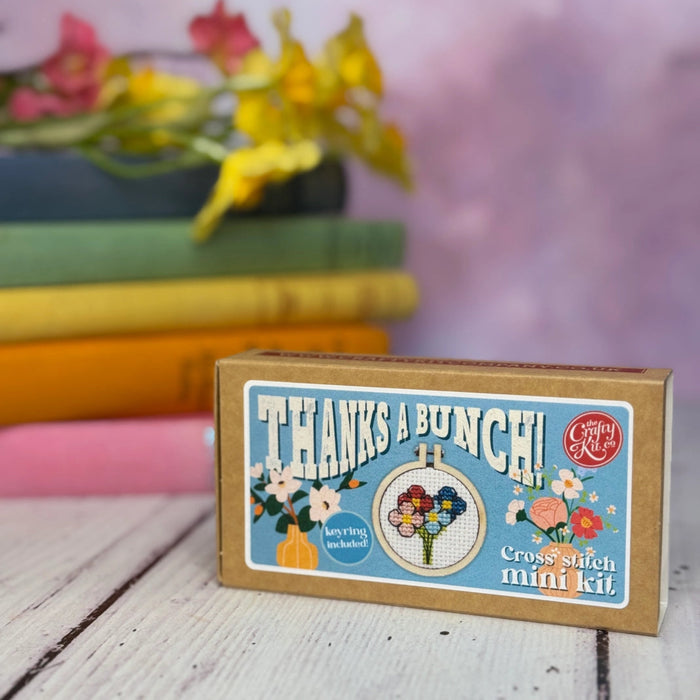 Cross-stitch mini kit box with floral design and text 'Thanks a Bunch!' on a wooden surface.
