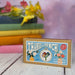 Cross-stitch mini kit box with floral design and text 'Thanks a Bunch!' on a wooden surface.