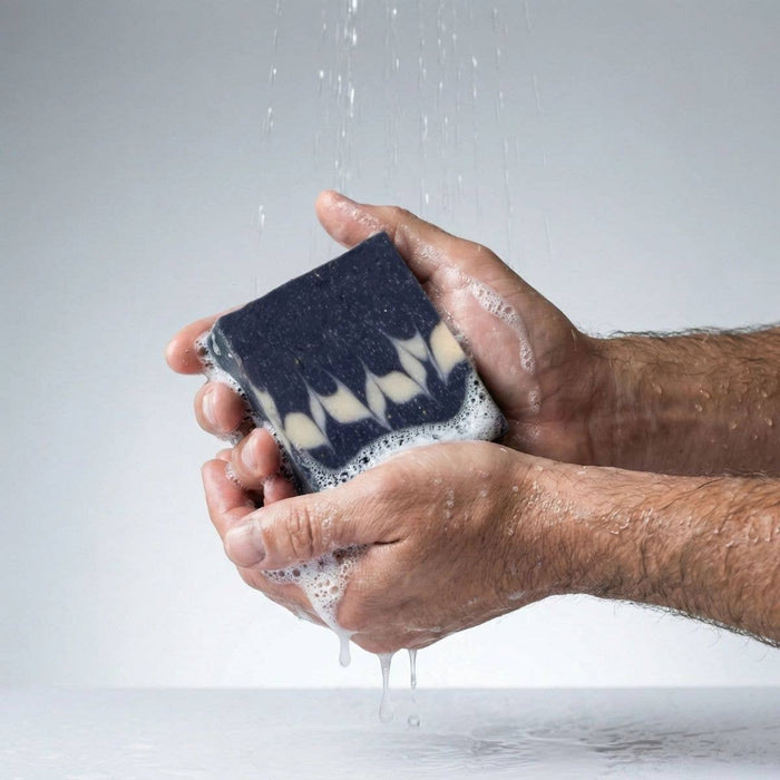 Hand holding a bar of soap under running water on a light gray background
